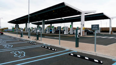 close-up of a modern electric charging station with solar panels and in the background several electric cars parked in its parking lot charging on their electric chargers.